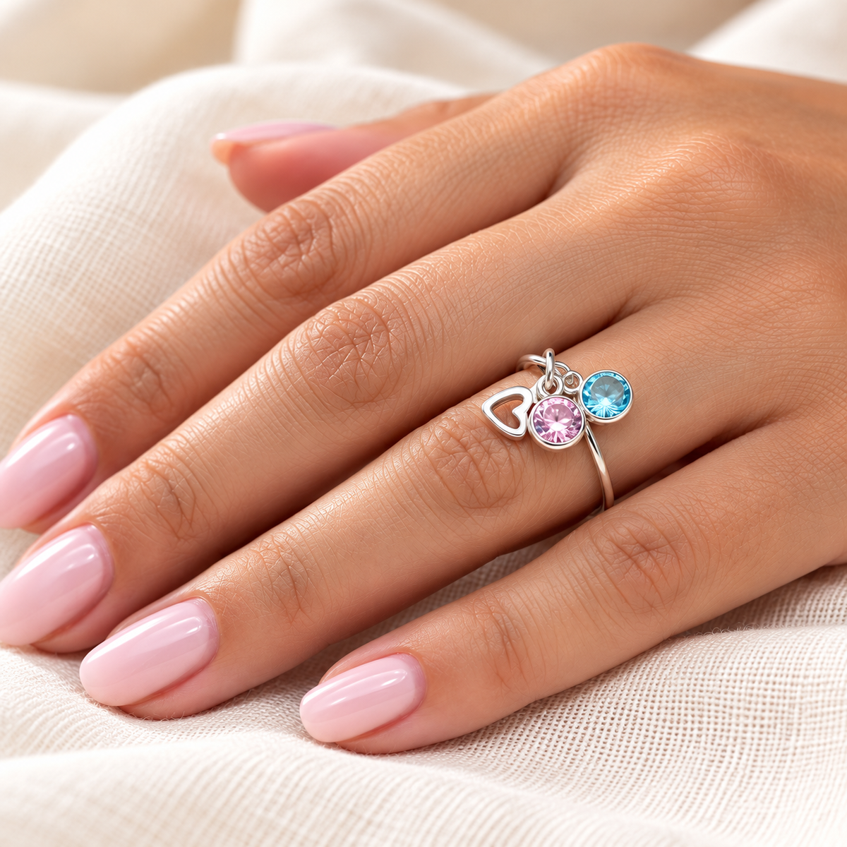 Anillo personalizable de plata con corazón y charms rosa y azul sobre una mano